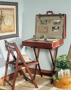 an open suitcase sitting on top of a wooden desk next to a chair and potted plant