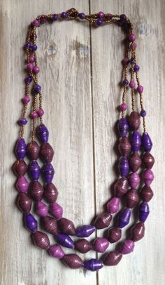 a purple and gold necklace on a white wooden surface with beads hanging from it's sides