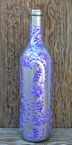 a purple and silver glass bottle sitting on top of a wooden table next to a fence