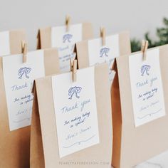 brown paper bags with blue ink on them are holding small thank you notes and clothes pins