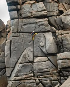 a man climbing up the side of a large rock face with a yellow rope attached to it