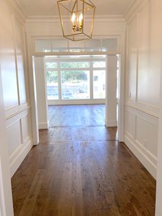 an empty room with hard wood flooring and white walls, light fixture hanging from the ceiling