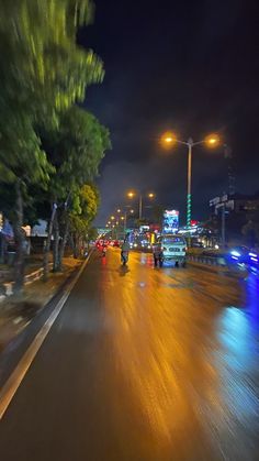 cars are driving down the street at night with lights shining on them and trees in the foreground