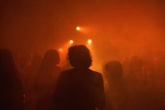 a group of people standing in the dark with their backs turned to the camera and lights behind them