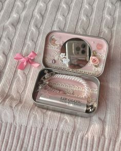 an open tin box with a pink bow on the side and a mirror in it