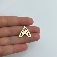 a hand holding a small gold plated pendant with an ornate design on the front