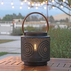 an outdoor lantern on a wooden table with string lights