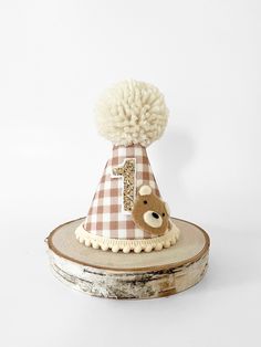 a brown and white hat with a teddy bear on it's head sitting on top of a piece of wood