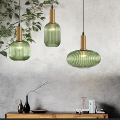 three green glass pendant lights hanging from the ceiling above a table with books and vases