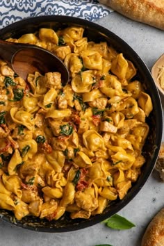 a skillet filled with pasta and spinach on top of a table next to bread