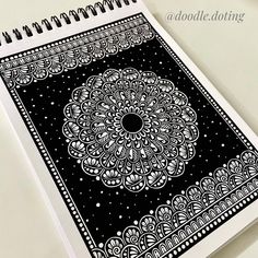 a black and white spiral notebook with an intricate design on the cover, sitting on a table