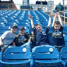 three young boys sitting in the stands at a baseball game with their hands up above their heads