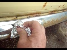 a hand is holding aluminum foil in front of a rusted car