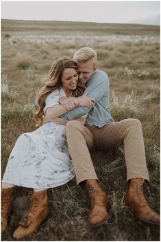 a man and woman sitting on the ground hugging each other in an open grassy field