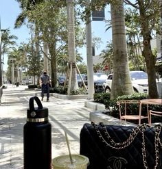 a woman walking down the sidewalk with her handbag and drink in front of her