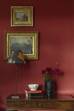 a room with red walls and pictures on the wall, including a table with flowers