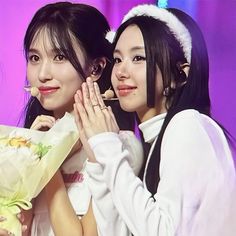 two women standing next to each other holding flowers