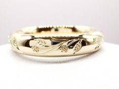 a gold wedding band with flowers and leaves on the inside, sitting on a white surface