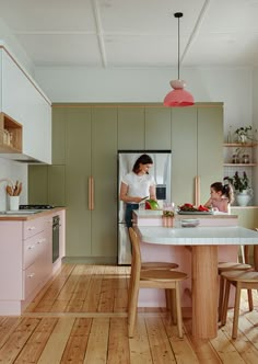 a woman and child are in the kitchen with pink cabinets, white countertops and wood floors