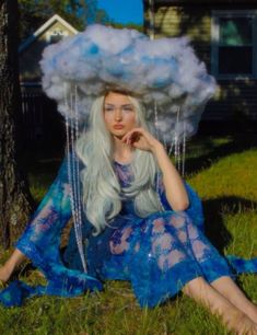 a woman sitting in the grass with a cloud on her head and chains hanging from it's sides