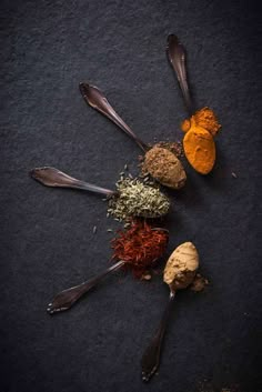 spoons filled with different types of spices on top of a black surface, next to each other