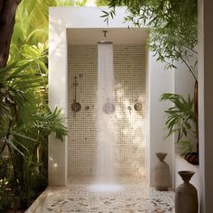 an outdoor shower with plants and potted trees in the backround, surrounded by foliage