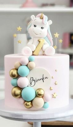 a pink and gold birthday cake with an unicorn on top