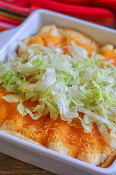 an enchilada with lettuce and cheese in a white dish on a wooden table