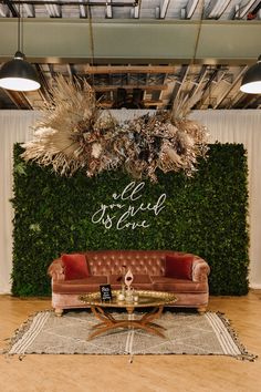 a couch sitting in front of a green wall with plants growing on top of it