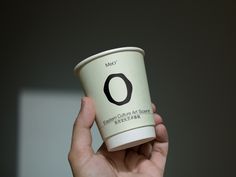 a person holding up a coffee cup with the word o on it's side