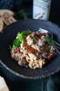 a black plate topped with pasta and meat next to bread on top of a table