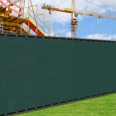 a large green wall with construction cranes in the background