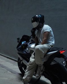 a man in white shirt riding on the back of a black motorcycle next to a wall