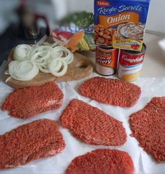 hamburger patties, onion rings and other ingredients on a cutting board next to a can of onion seasoning