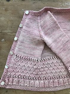 a pink knitted sweater sitting on top of a wooden floor next to a pair of scissors