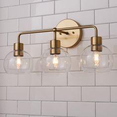 three clear globe lights are mounted on the wall above a white tile backsplash