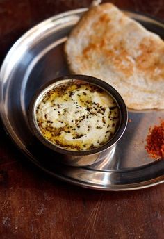 a silver plate topped with food next to a piece of bread on top of a wooden table