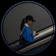 a woman in a blue jacket is on an escalator and looking at her cell phone