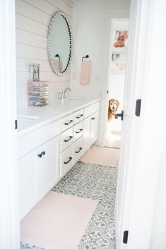 a white bathroom with a dog in the mirror and pink rugs on the floor