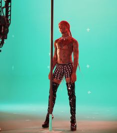 a shirtless man standing in front of a green screen wearing black boots and stockings