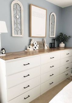 a white dresser sitting in a bedroom next to a lamp and pictures on the wall