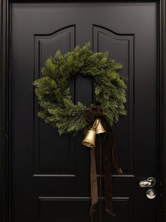 a black door with a wreath and bells hanging on it's front door handle