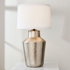 a silver vase with a white lamp on top of it next to a wall in a room