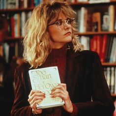 a woman holding a book in front of a bookshelf