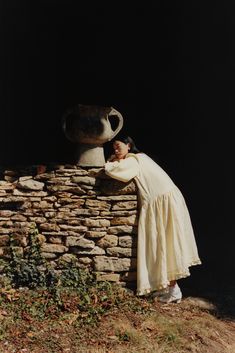 a woman leaning against a stone wall with a vase on it's back end