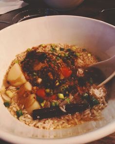 a white bowl filled with rice, meat and veggies on top of a wooden table