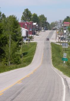 an empty street with houses and trees on both sides in the distance is a small town