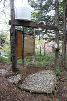 an outdoor toilet in the woods with a bucket hanging from it's roof and some rocks on the ground