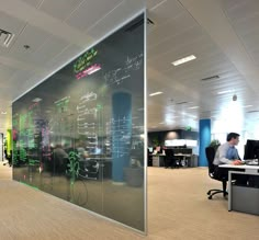 an office with glass walls and people working on their laptops in the middle of the room