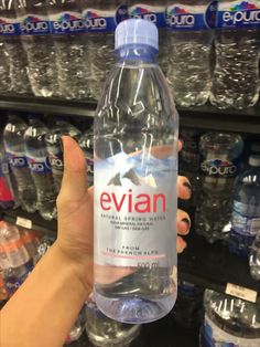 a hand holding a bottle of evian water in front of shelves of bottled water